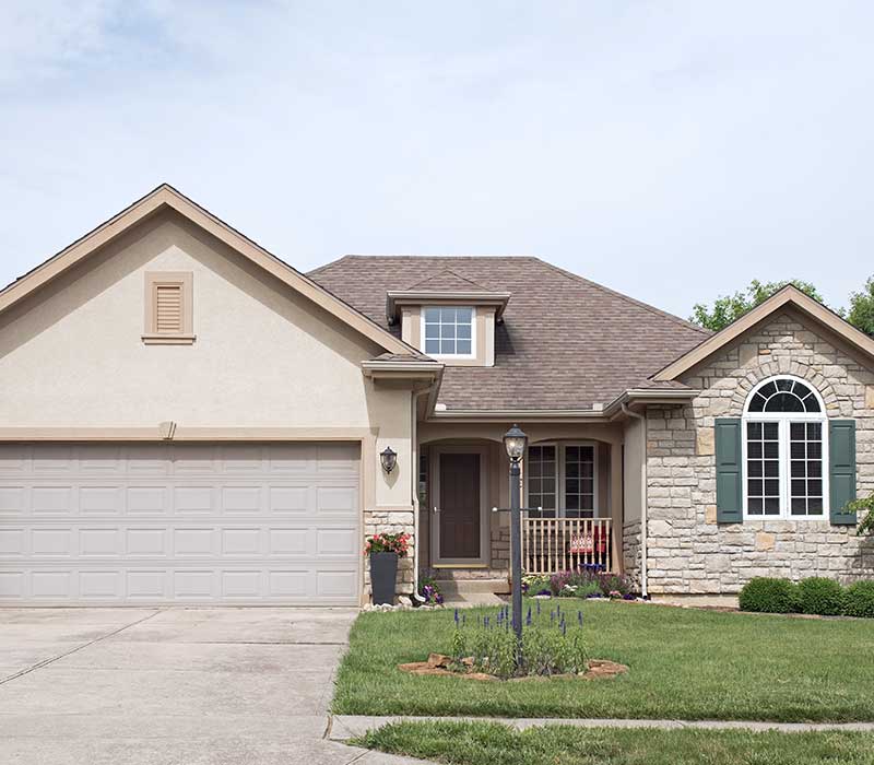 Front view of a typical, light brown mid-class home with brown shingles on its roof